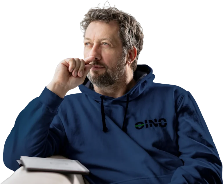 Mann mit nachdenklichem Blick trägt dunkelblauen Hoodie mit EINO-Logo, sitzt mit Tablet auf der Couch