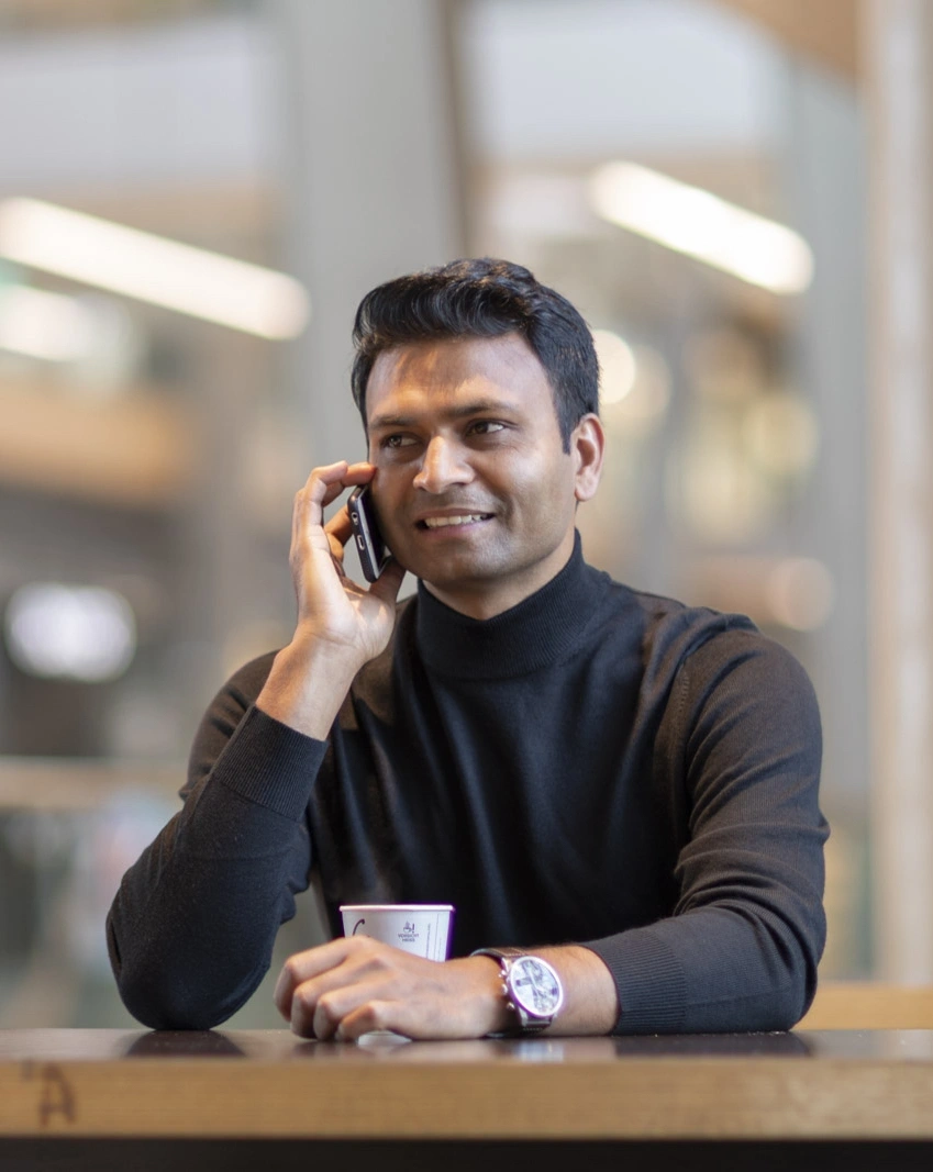 Man, smiling, wearing a black longsleeve, sitting at a desk and talking on the phone
