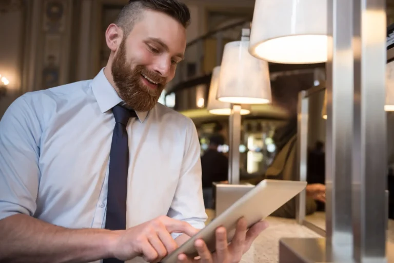 Ein Mann in Businesskleidung steht in der Hotellobby und schaut auf das Tablet, was er in den Händen hält