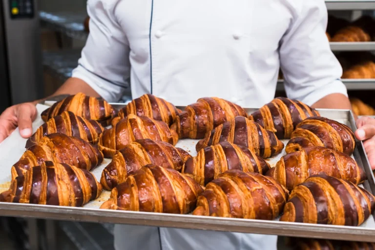 Eine Küchenhilfe in weißer Kleidung hält ein Tablett mit ofenfrischen Croissants