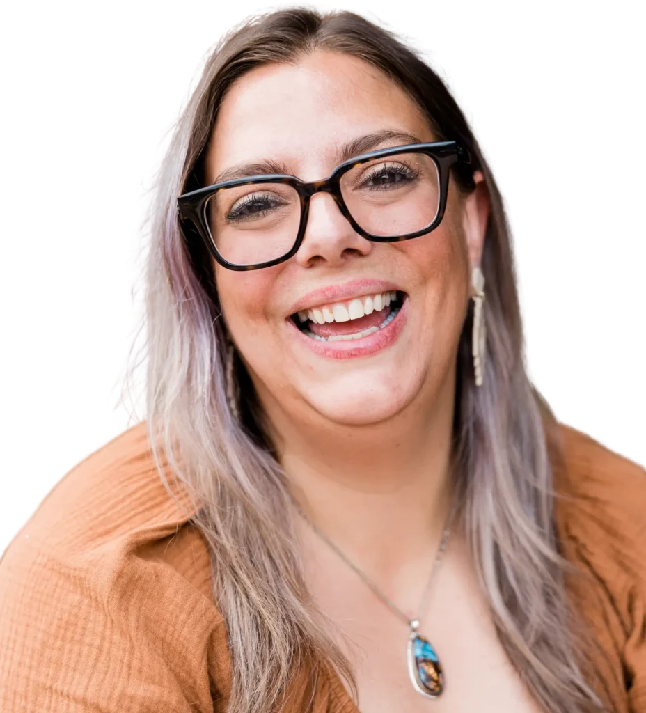 Woman with long hair, large glasses and brown blouse laughs openly into the camera