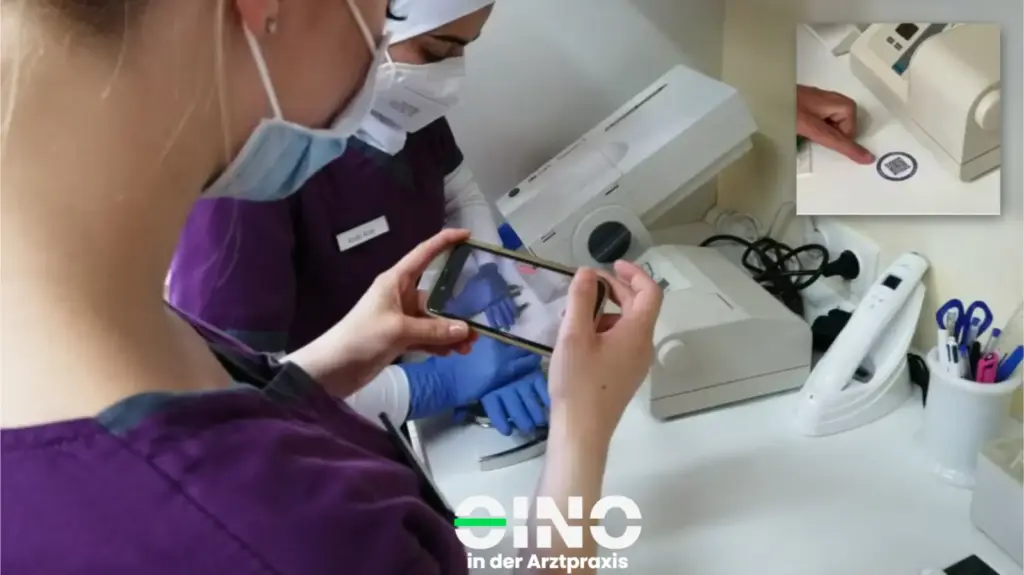 Zwei ZFAs stehen am Tisch und scannen mit dem Handy einen QR-Code