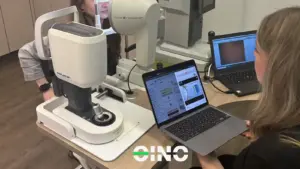 Eine Augenoptikerin macht eine Messung mit einer Kundin und schaut auf den Laptop